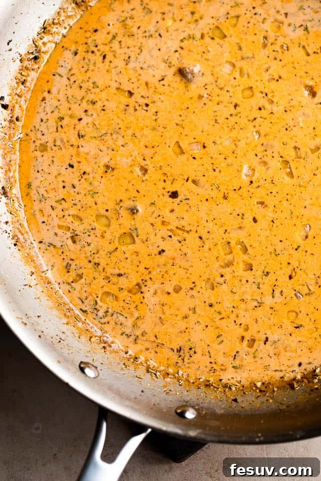 A stainless steel skillet filled with a simmering creamy tomato sauce, rich with onions and garlic, ready to receive the cooked tilapia.