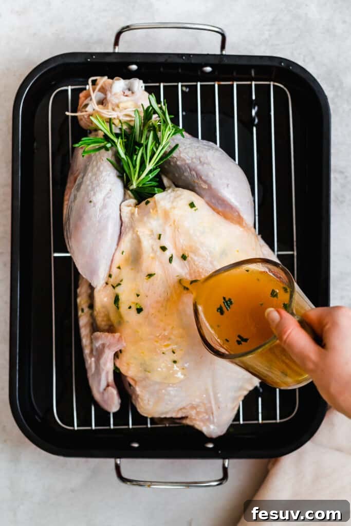 Uncooked turkey in a roasting pan, with broth being poured over it.