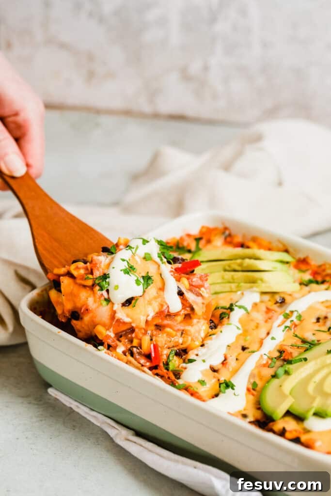 Cheesy Chicken Enchilada Delight 3 A wooden spoon scooping into a freshly baked Chicken Enchilada Casserole, showcasing the rich layers of chicken, beans, corn, and melted cheese.