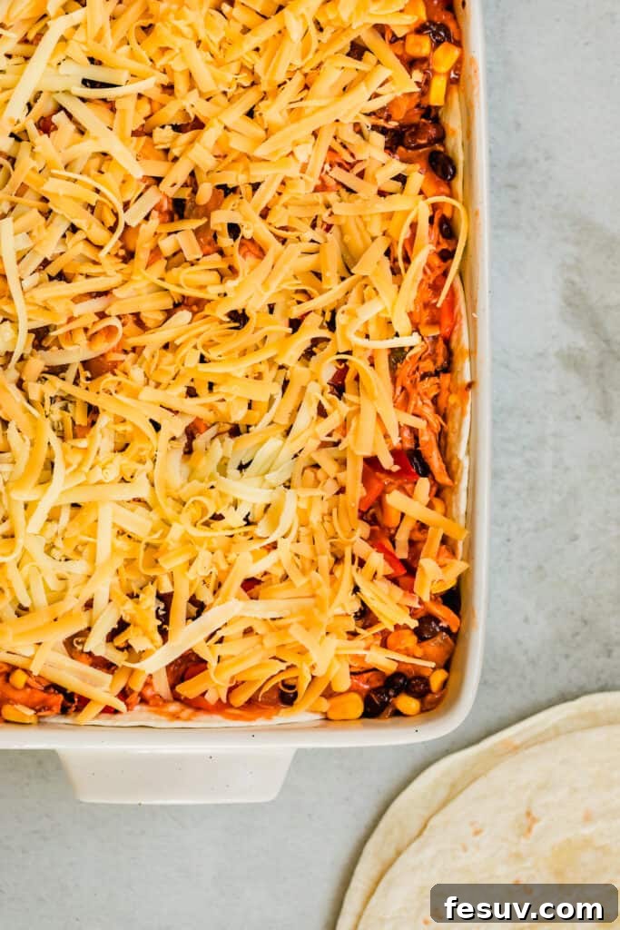 Cheesy Chicken Enchilada Delight 5 A vibrant and cheesy Chicken Enchilada Casserole in a baking pan, with two soft flour tortillas placed beside it, ready for layering.