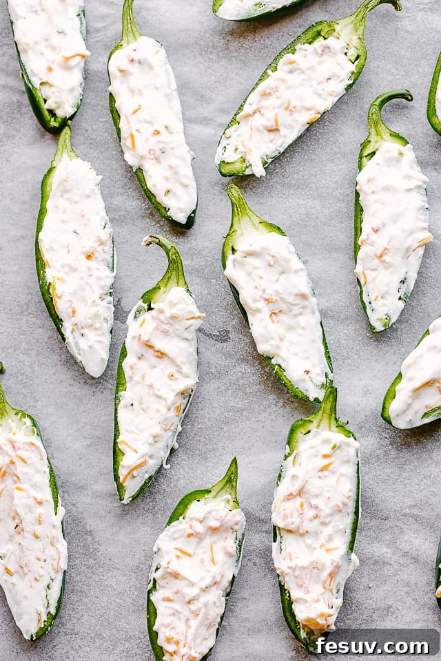 Creamy, spicy, crunchy Bacon Wrapped Jalapeño Poppers are stuffed with cheese and wrapped in bacon. The perfect Super Bowl food idea! Raw jalapeno halves, stuffed with creamy shredded cheese filling, ready for bacon wrapping.