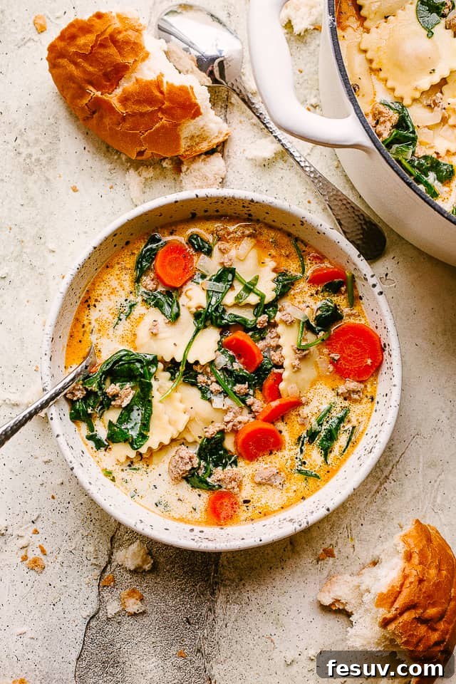 A bowl with creamy ravioli soup. Torn up bread is placed near the bowl.