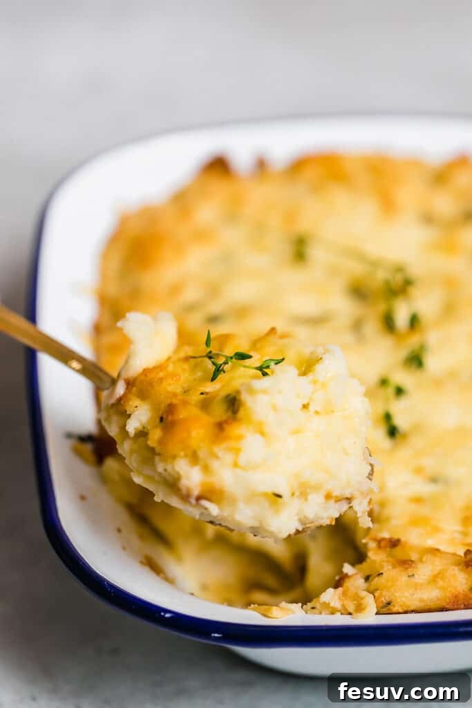 Close up side shot of scooping out creamy baked mashed potatoes from a white baking dish, showing the golden cheesy topping and fluffy interior.
