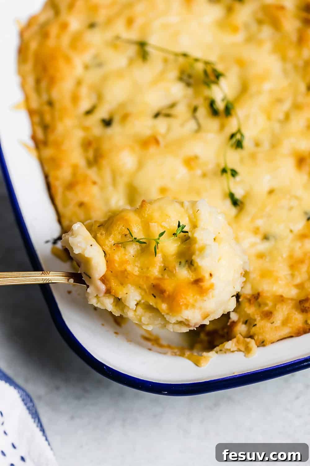 A serving spoon lifting a portion of warm, creamy baked mashed potatoes out of a casserole dish, showing the gooey cheese.