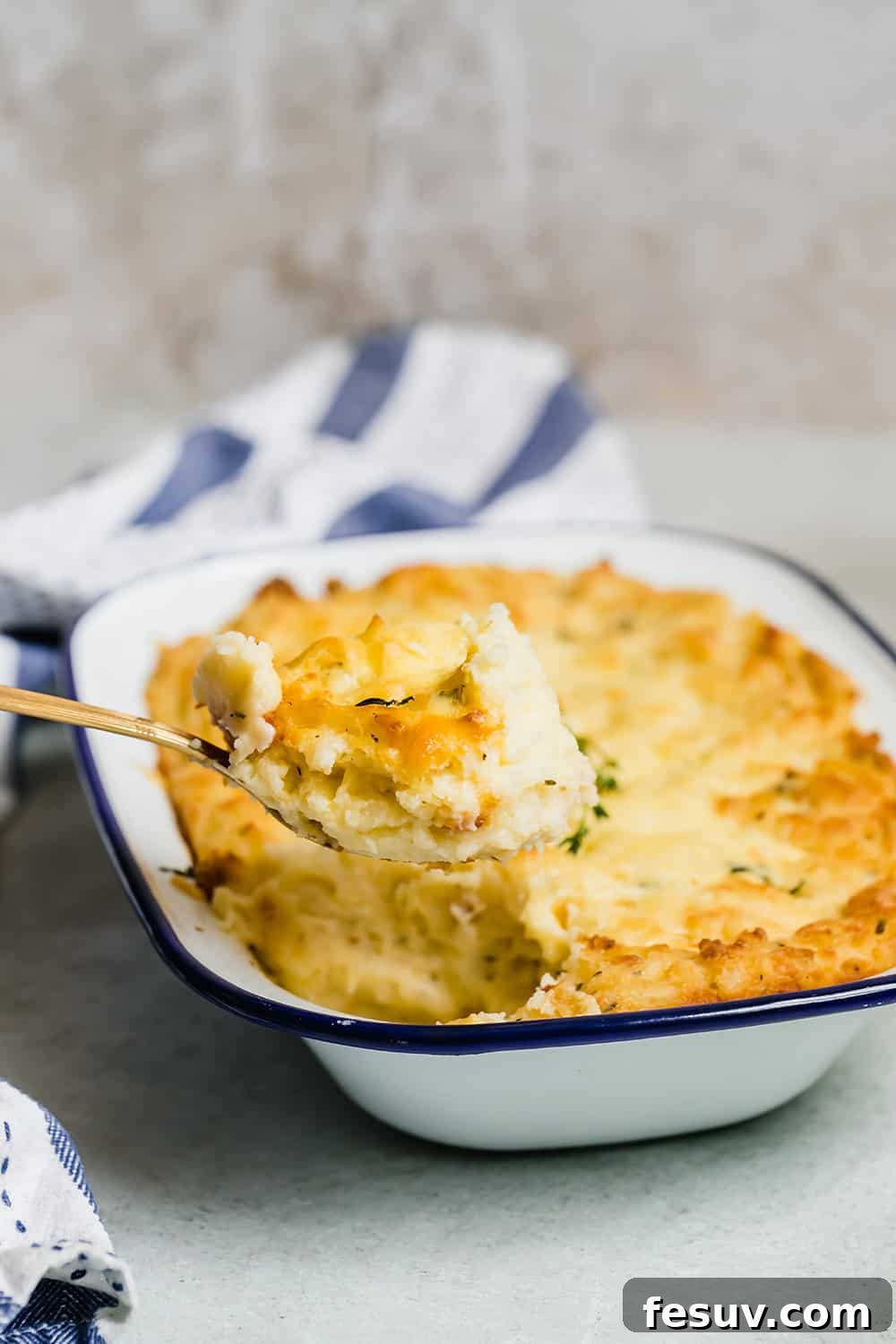 A spoon scooping a generous portion of creamy mashed potatoes from a white serving dish, ready to be enjoyed.