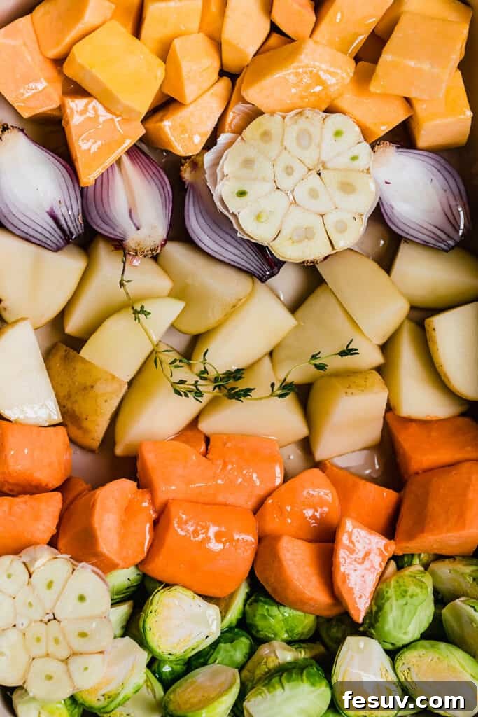 A close-up view of freshly chopped winter root vegetables, including orange butternut squash cubes, halved green brussels sprouts, white potato quarters, and small red onion pieces, ready for roasting.