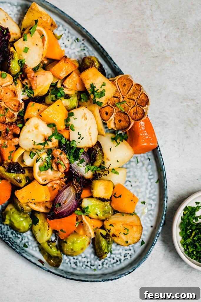 A generous serving of golden-brown roasted root vegetables, including potatoes, butternut squash, and brussels sprouts, garnished with fresh herbs, presented on a round blue ceramic platter, ready to be enjoyed.