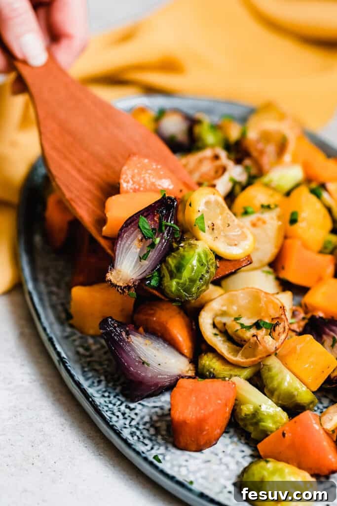 A wooden serving spoon gently scoops a portion of hot, golden-brown roasted vegetables off a vibrant blue serving platter, highlighting the texture and readiness of the dish.