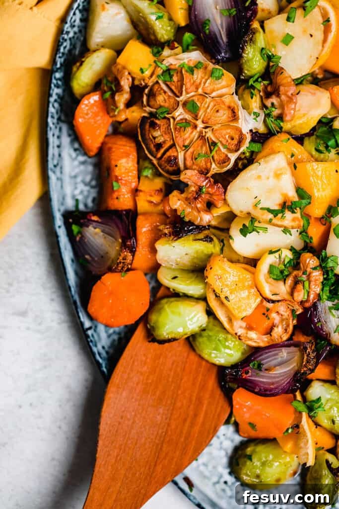 A close-up of a wooden spoon resting on a generous pile of golden roasted vegetables on a blue serving platter, garnished with fresh herbs, ready to be served or enjoyed.
