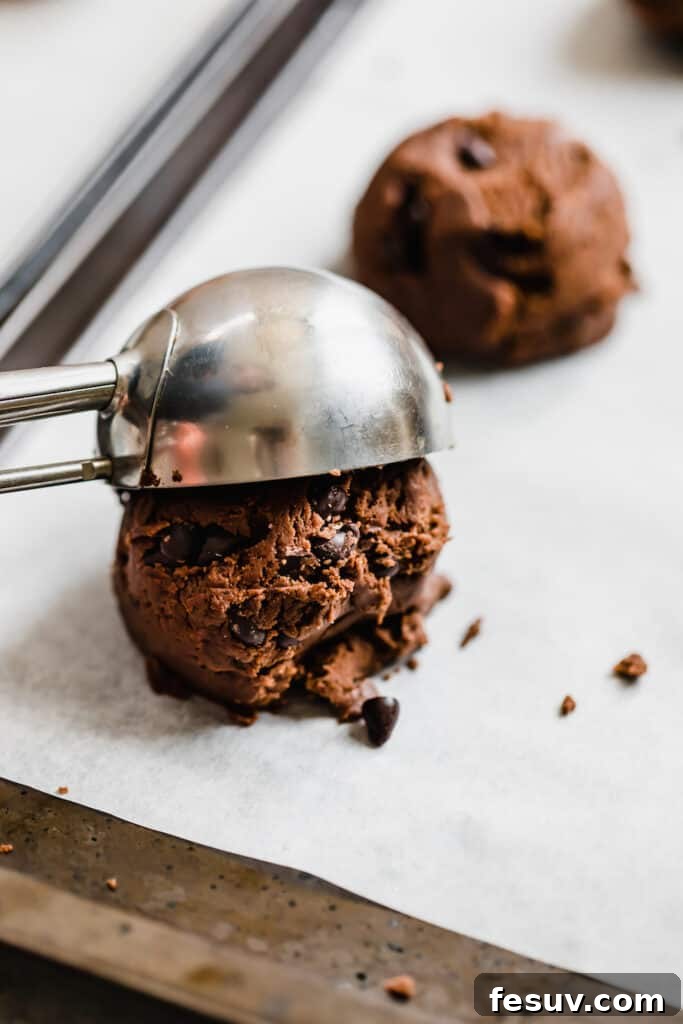 A Metal Ice Cream Scoop Releasing a Ball of Chocolate Sugar Cookie Dough onto a baking sheet