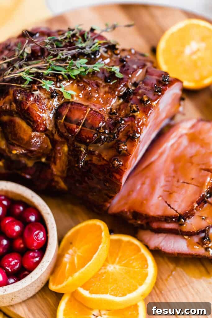 Slices of Christmas Ham on a Circular Wooden Surface with Assorted Fruits and herbs for garnish.