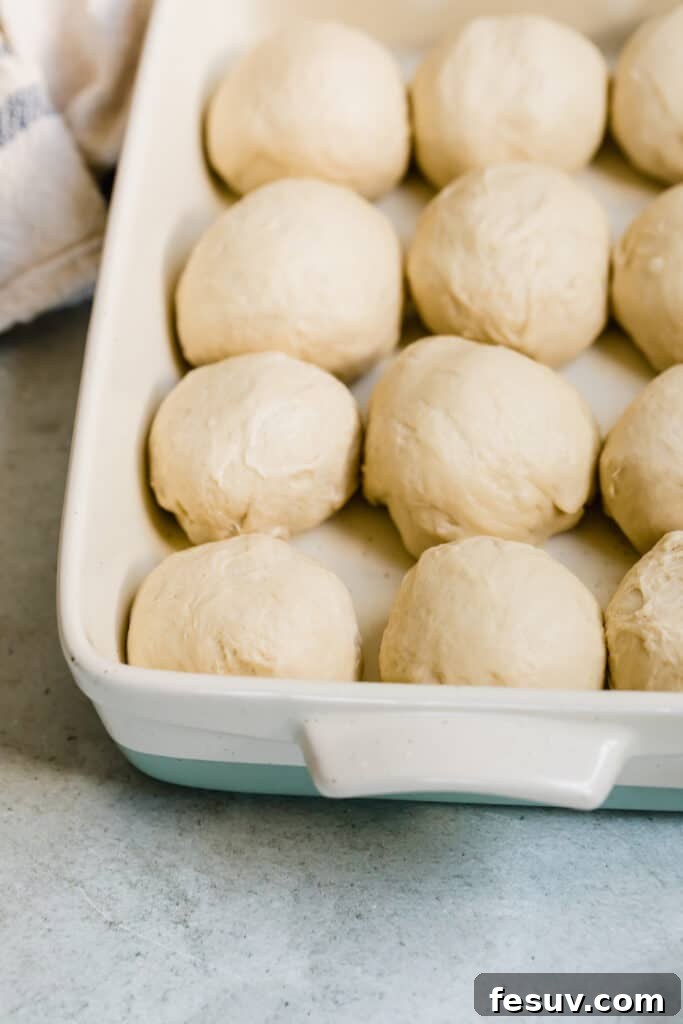 Neatly arranged balls of unbaked dinner roll dough in a baking pan, prior to rising
