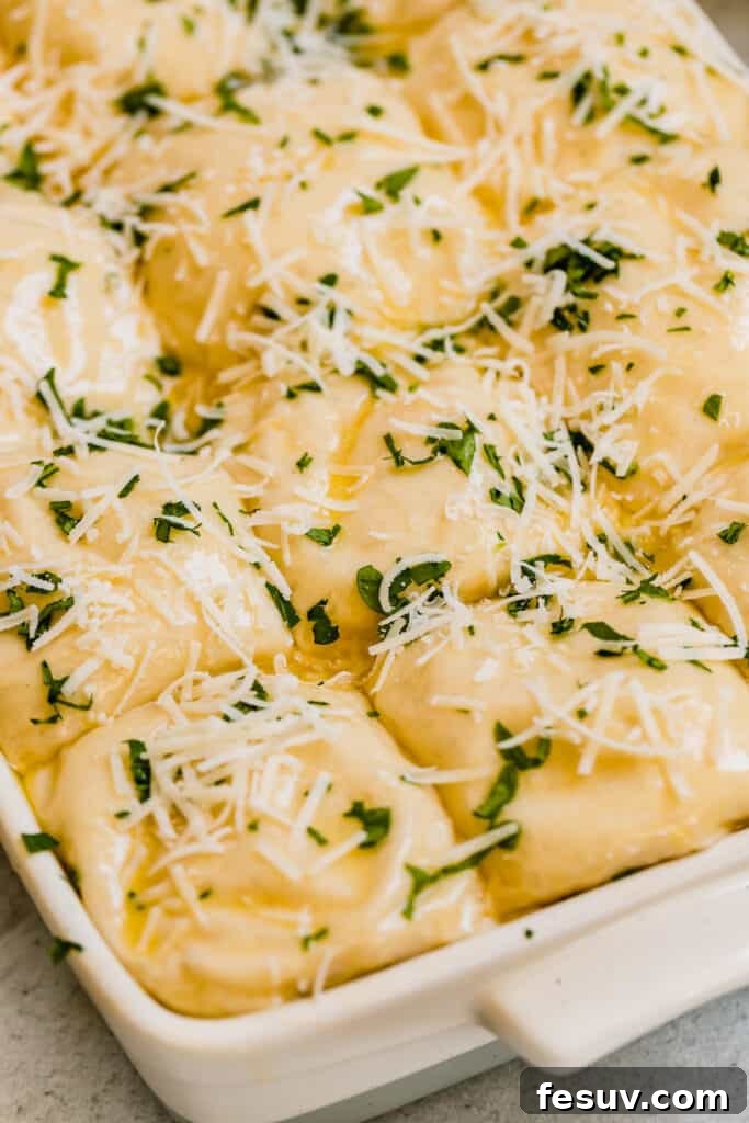 Unbaked Parmesan Dinner Roll dough topped with cheese and parsley in an oven-ready pan