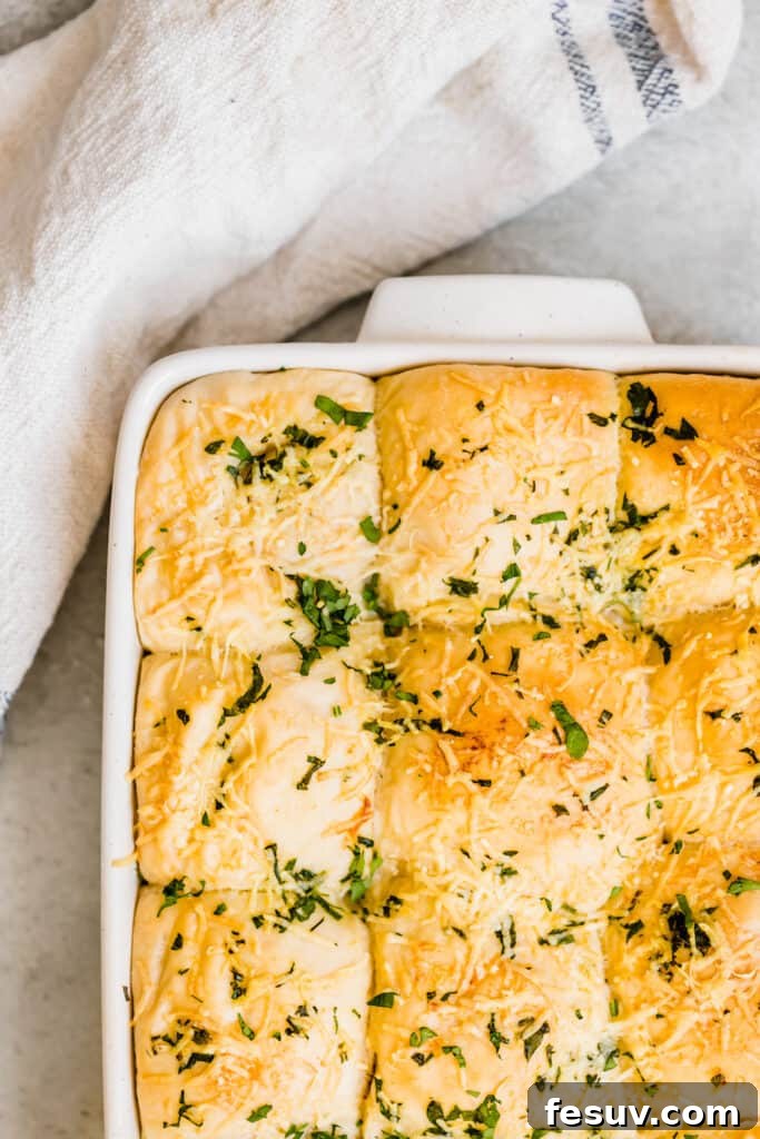 A pan overflowing with freshly baked dinner rolls, richly seasoned with Parmesan cheese and fresh parsley