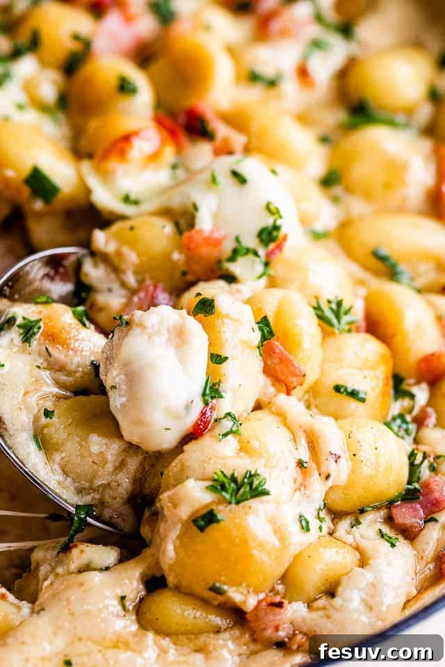 Ultimate Bacon Gnocchi Bake 3 Close-up shot of a spoon scooping into a creamy gnocchi casserole, showing the rich texture and ingredients.
