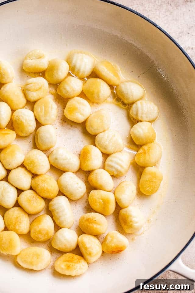 Ultimate Bacon Gnocchi Bake 4 Close-up shot of gnocchi frying in a white skillet until golden brown and crispy.
