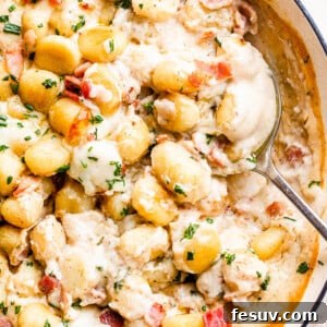 A serving spoon lifting a portion of creamy Gnocchi and Bacon Casserole from a baking dish, showcasing the tender gnocchi and rich sauce.