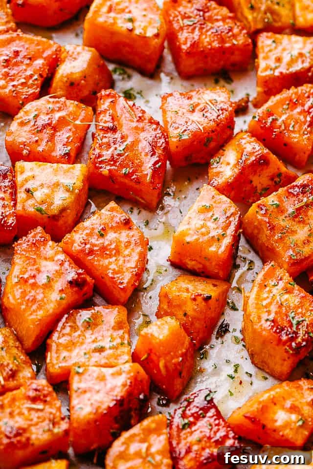 Roasted Sweet Potatoes are a sweet and savory side dish of cubed sweet potatoes that are perfectly seasoned and glazed with butter, honey, and garlic! Overhead shot of perfectly roasted garlic honey sweet potatoes on parchment paper, ready to serve.