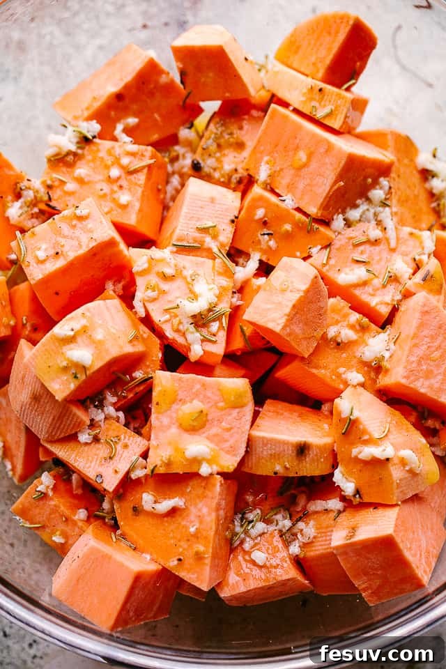 Roasted Sweet Potatoes are a sweet and savory side dish of cubed sweet potatoes that are perfectly seasoned and glazed with butter, honey, and garlic! Overhead shot of freshly chopped raw sweet potato cubes in a large mixing bowl, ready for seasoning and roasting.