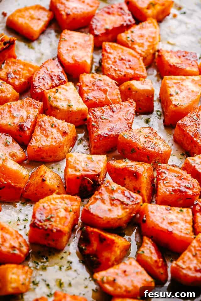 Roasted Sweet Potatoes are a sweet and savory side dish of cubed sweet potatoes that are perfectly seasoned and glazed with butter, honey, and garlic! Close-up overhead shot of garlic honey roasted sweet potatoes, garnished with fresh herbs, on a baking sheet lined with parchment paper.