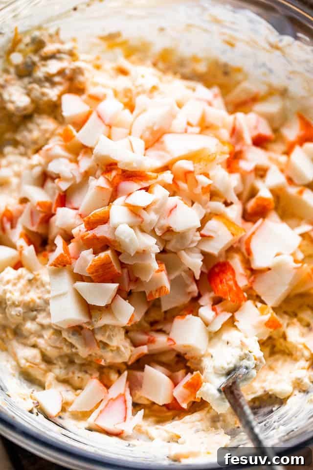 Mixing lump crab meat into the creamy base of the hot crab dip in a glass bowl.