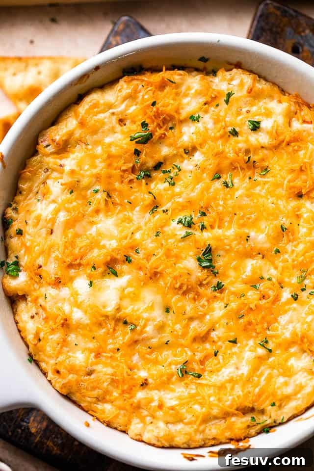 Overhead shot of a white skillet filled with hot, bubbling crab dip, garnished with fresh parsley.