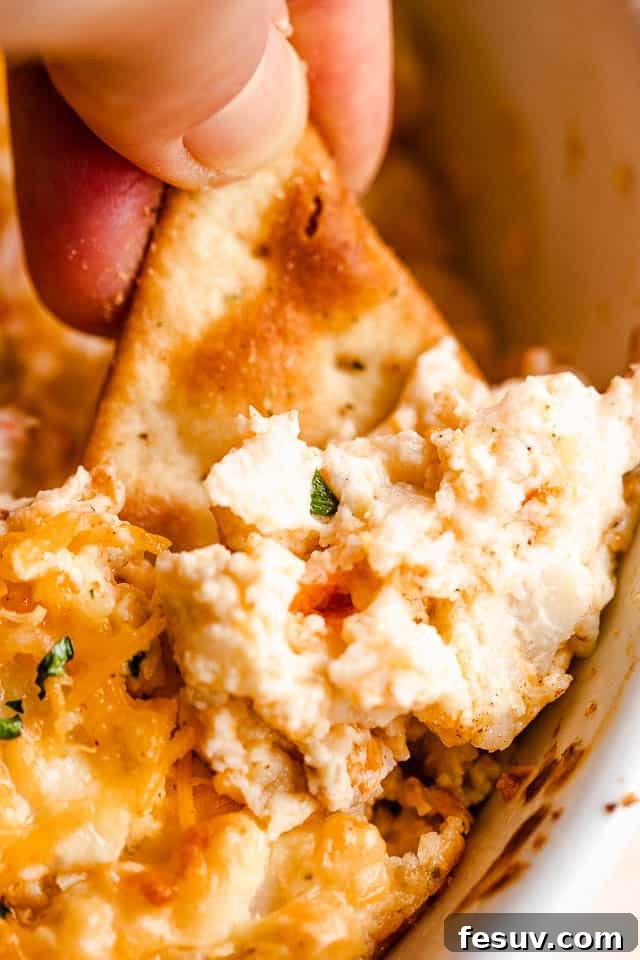 Pita chip being dipped into hot crab dip, showing the melted cheese pull.