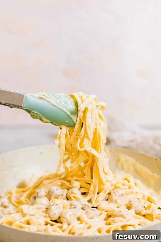 A Pair of Tongs Grabbing a Bunch of Fettuccine Noodles Covered in Alfredo