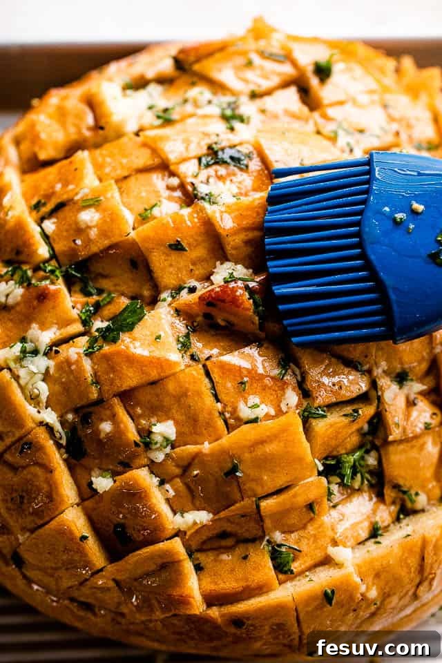 Ultimate Cheesy Garlic Sharing Loaf 4 a pastry brush coating a crosshatched loaf of bread with melted butter, garlic, and parsley