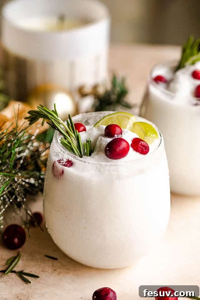 Two elegant drinking glasses filled with creamy white frozen margaritas, garnished with fresh lime slices, rosemary sprigs, and ruby-red cranberries, set against a festive backdrop.