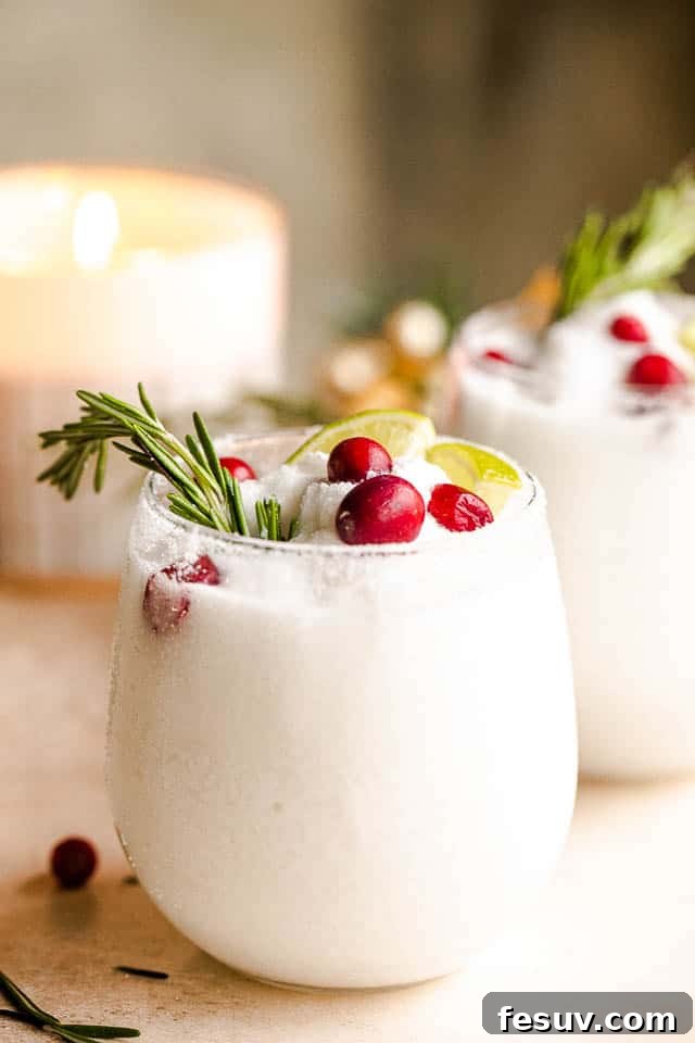 A festive spread featuring multiple drinking glasses filled with white frozen margaritas, adorned with lime slices, cranberries, and rosemary sprigs, creating a vibrant holiday display.