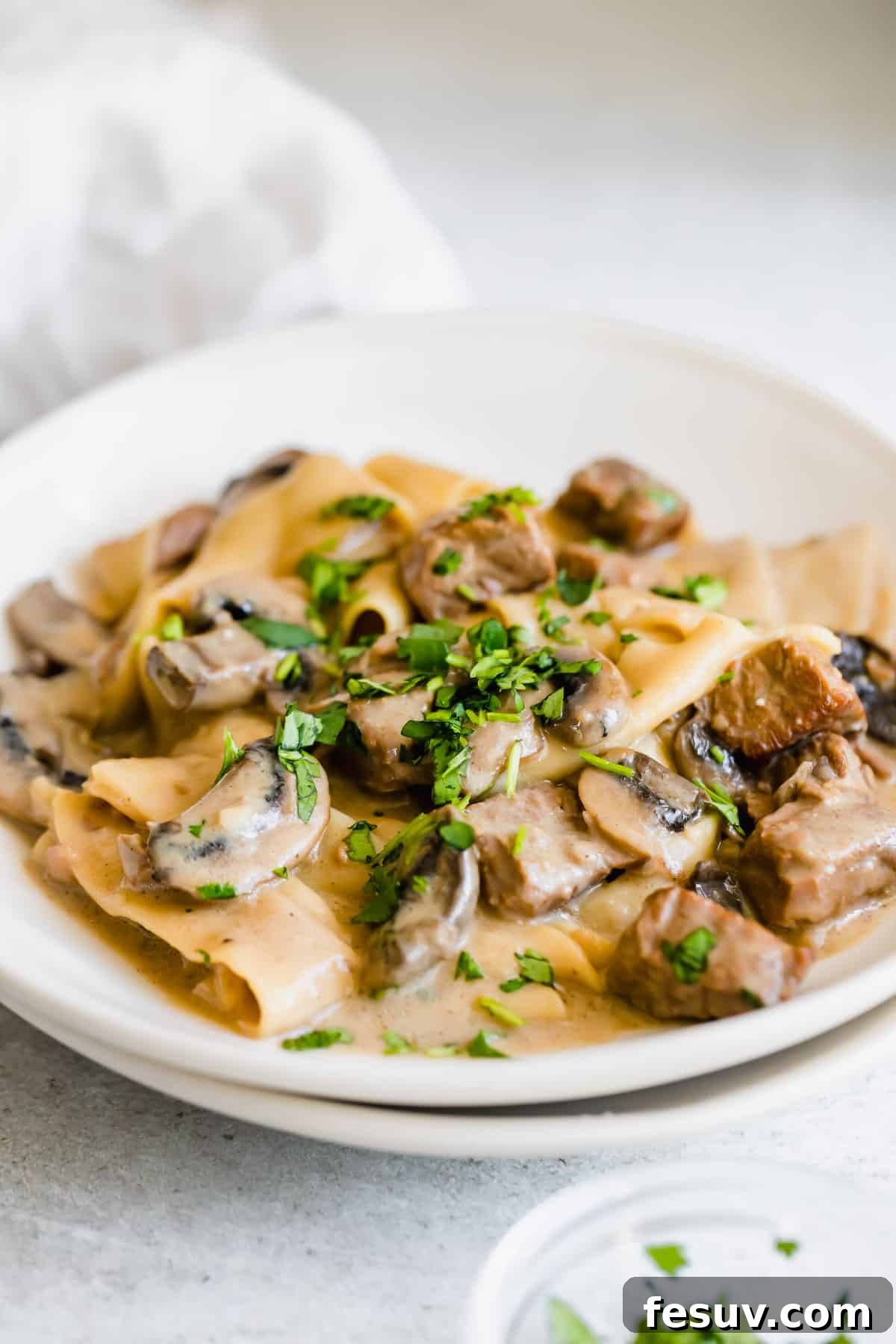 Effortless Creamy Instant Pot Beef Stroganoff 13 A Plate of Beef Stroganoff Next to a Small Bowl of Chopped Parsley, ready for garnishing.
