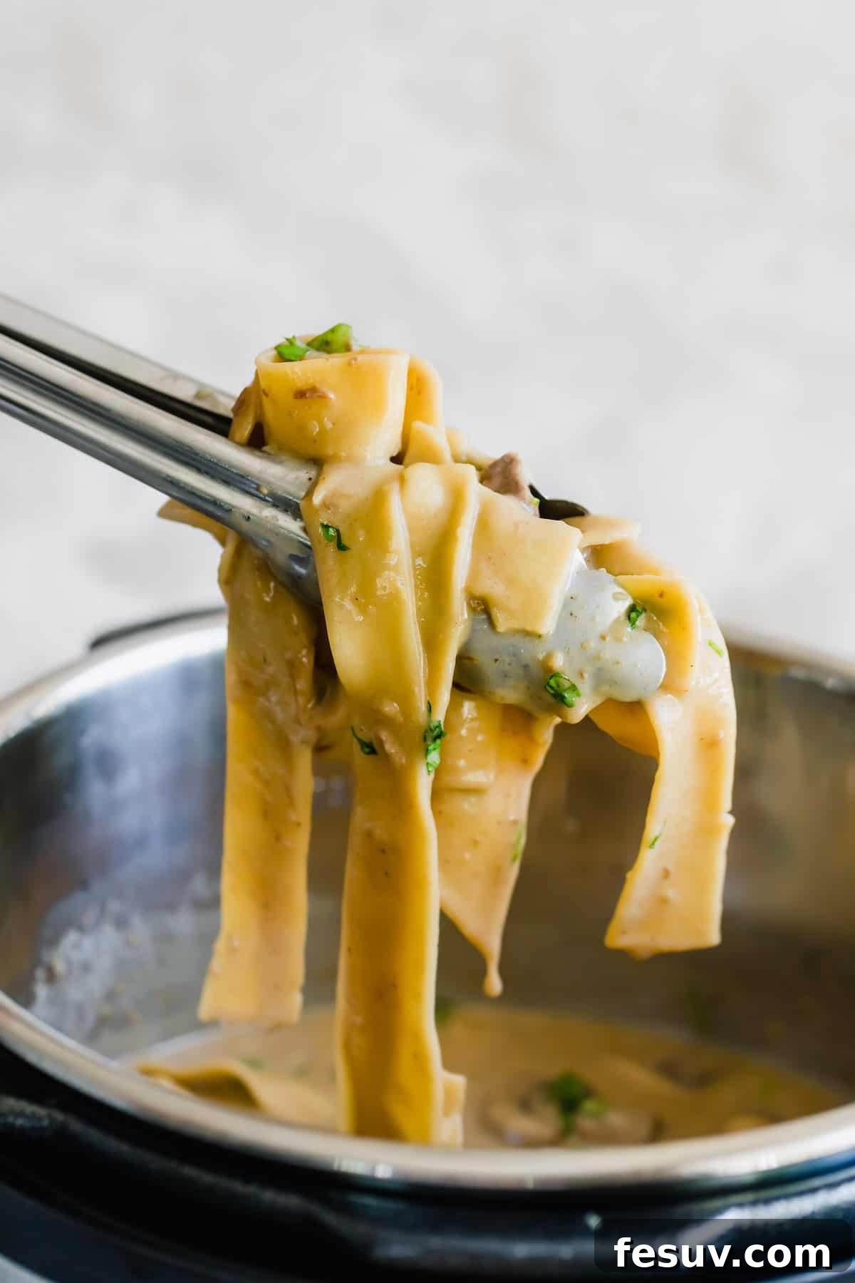 Effortless Creamy Instant Pot Beef Stroganoff 4 A Pair of Tongs Pulling a Scoop of Creamy Beef Stroganoff Out of the Instant Pot, showing the steam and rich texture.