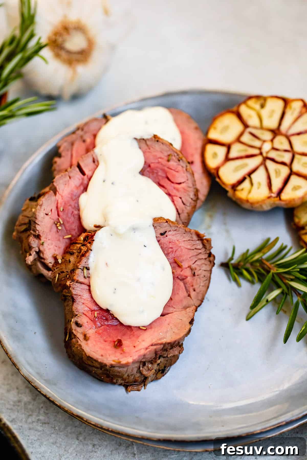 Perfectly cooked slices of Roast Beef Tenderloin with a dollop of creamy Horseradish Sauce on a cutting board, garnished with fresh herbs.
