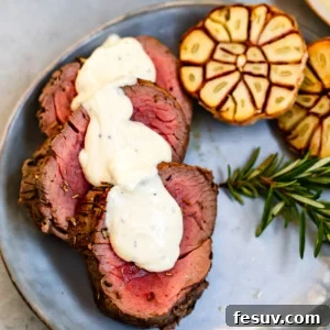 Three slices of juicy Roast Beef Tenderloin topped with homemade Horseradish Sauce, garnished with fresh herbs.