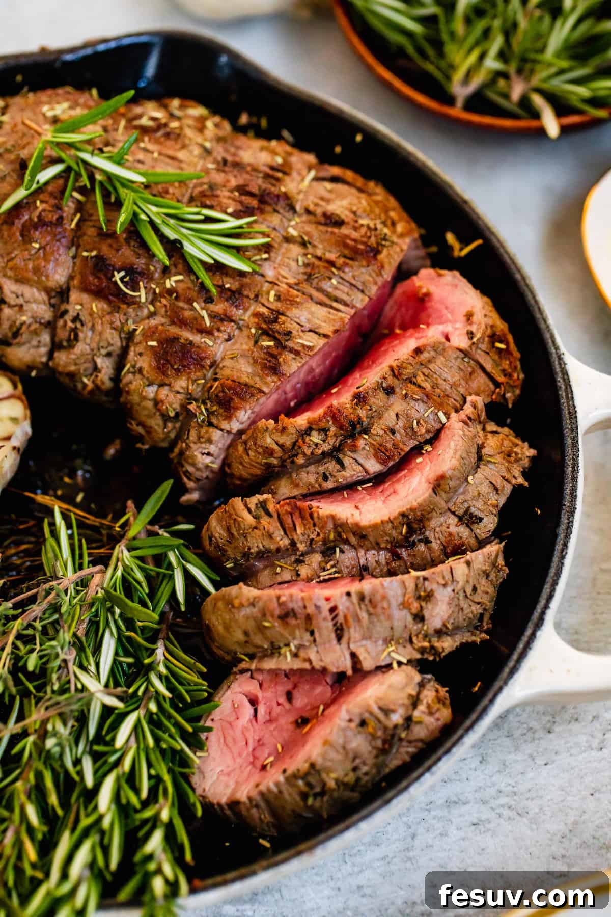 Thick slices of perfectly cooked homemade roast beef tenderloin inside a metal skillet, showing its juicy pink interior.