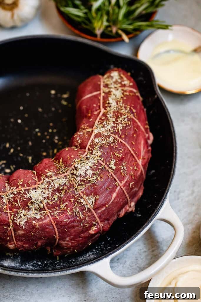 A close-up shot of a beef tenderloin generously covered in a savory blend of dried seasonings, ready for cooking.