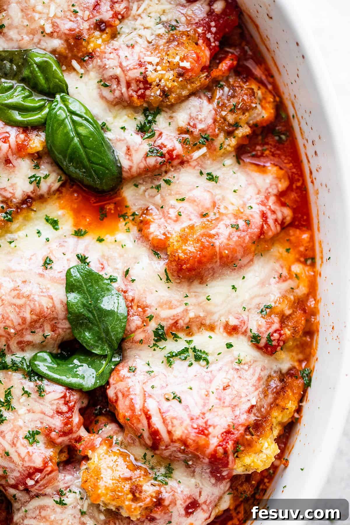 Crispy Pork Parmesan 2 close up overhead shot of baked pork parmigiana topped with melted cheese and basil leaves.