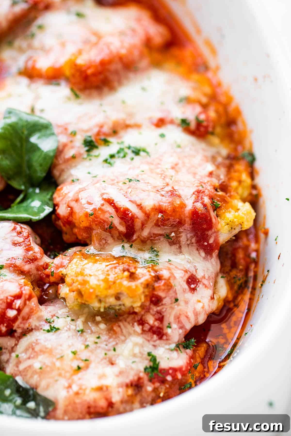 Crispy Pork Parmesan 5 close up side shot of baked pork parmigiana topped with melted cheese and basil leaves.