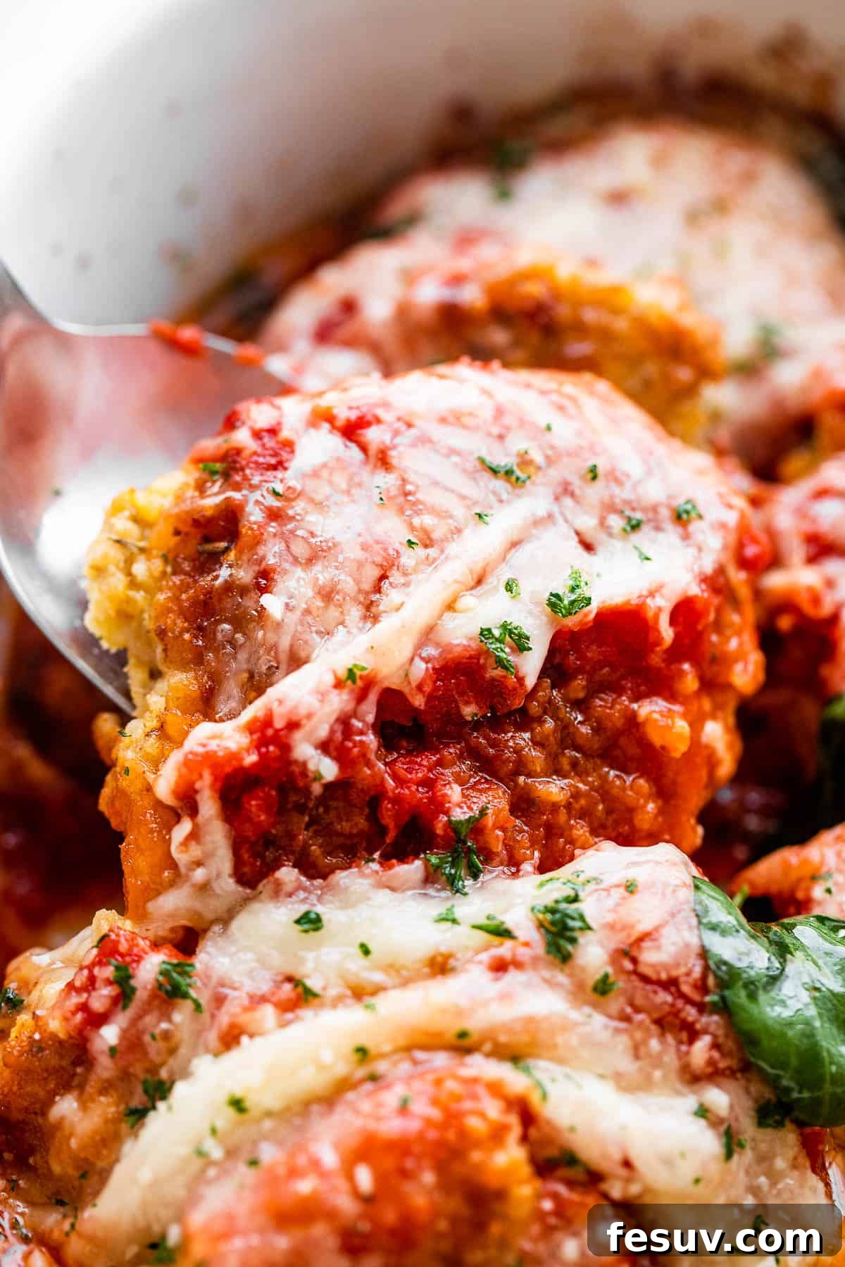 Crispy Pork Parmesan 6 spooning out baked pork parmigiana medallions from baking dish.