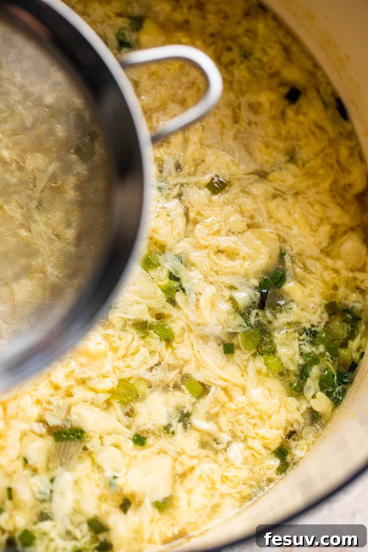 Forming Egg Ribbons in Soup Dropping whisked egg into simmering chicken broth through a fine mesh sieve to create delicate ribbons.