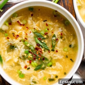 Overhead shot of a bowl with egg drop soup garnished with green onions and red pepper flakes