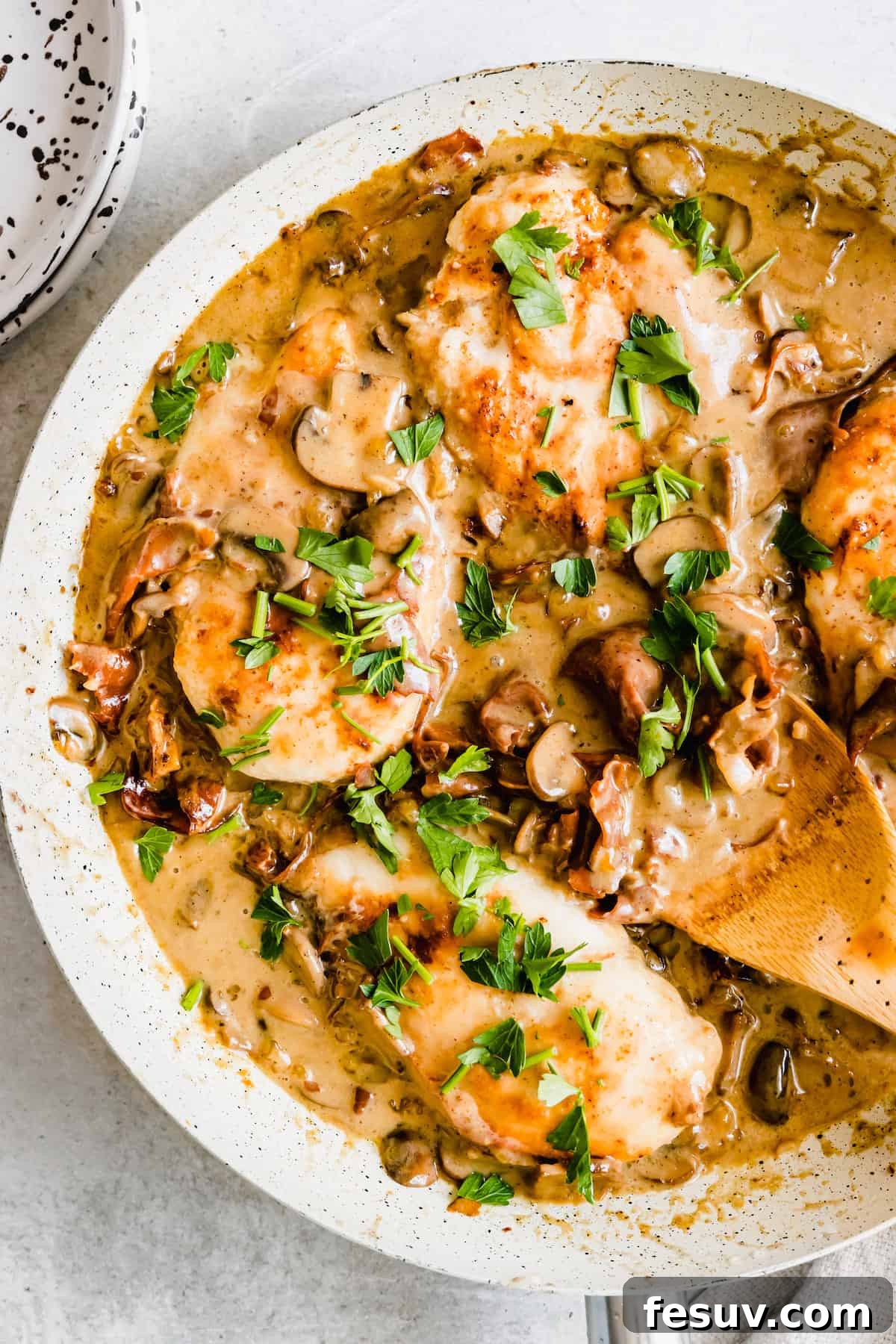 Rich Creamy Chicken Marsala 2 Chicken marsala in a white pan with a wooden spoon