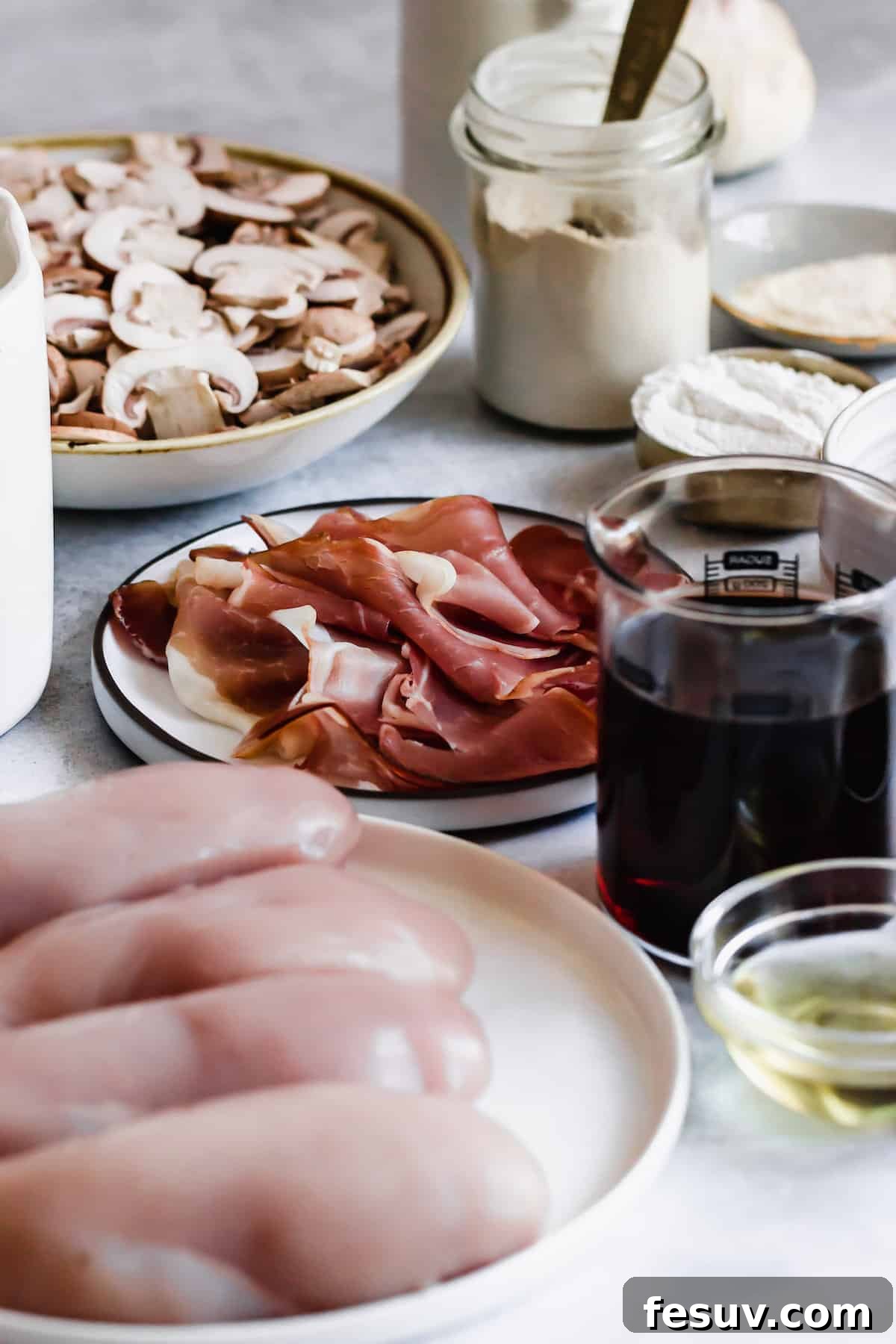 Rich Creamy Chicken Marsala 4 A plate of sliced white mushrooms, a plate of proscuitto, a cup of flour, and a cup of marsala wine.