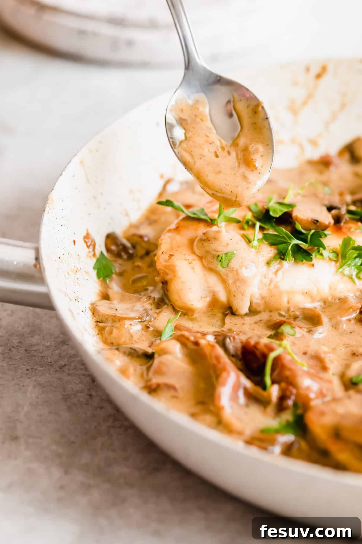 Rich Creamy Chicken Marsala 8 A spoon pouring creamy sauce over a piece of chicken with fresh herbs sprinkled on top.