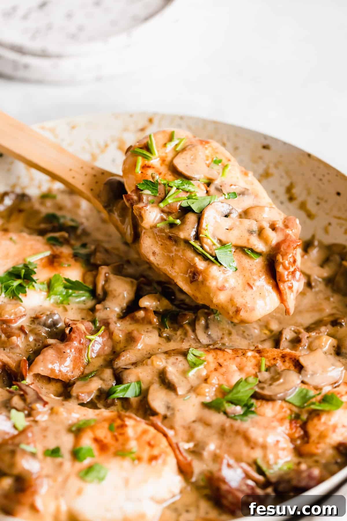 Rich Creamy Chicken Marsala 9 A piece of chicken in creamy marsala sauce on a wooden serving spoon.
