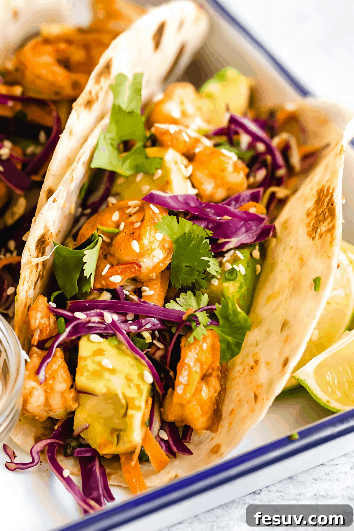 My easy shrimp tacos recipe with Asian cabbage slaw is guaranteed to be a new favorite. The classic flavors of a warm shrimp taco blend amazingly with the fresh, crunchy slaw in warm tortillas! A Platter Holding Four Shrimp Tacos and a Dish of Dressing