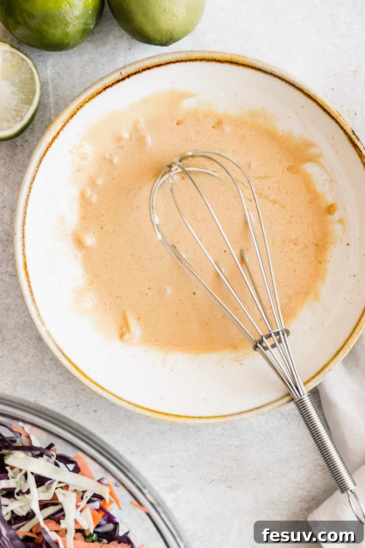 My easy shrimp tacos recipe with Asian cabbage slaw is guaranteed to be a new favorite. The classic flavors of a warm shrimp taco blend amazingly with the fresh, crunchy slaw in warm tortillas! Asian Dressing in a White Bowl with a Whisk