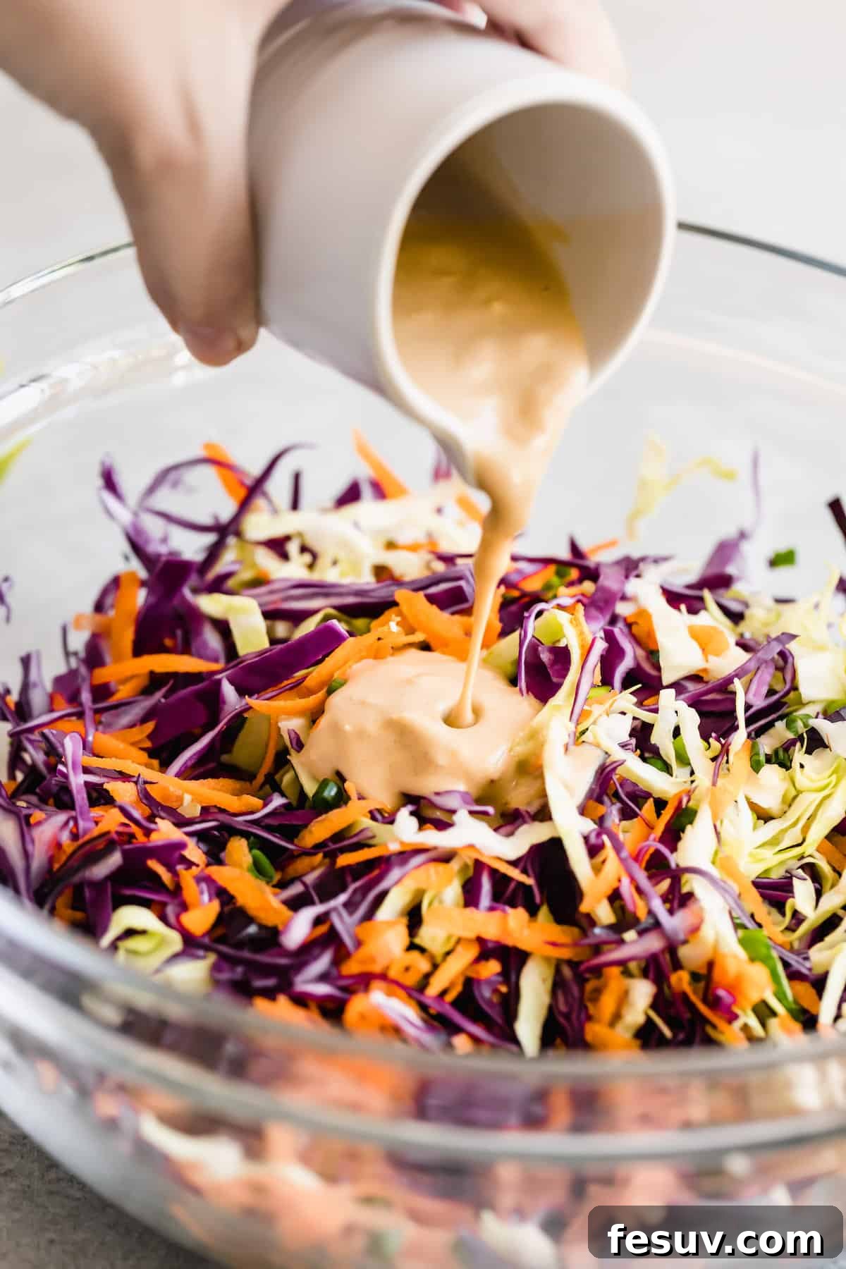 My easy shrimp tacos recipe with Asian cabbage slaw is guaranteed to be a new favorite. The classic flavors of a warm shrimp taco blend amazingly with the fresh, crunchy slaw in warm tortillas! Asian Dressing Being Poured Over the Cabbage Slaw Mixture