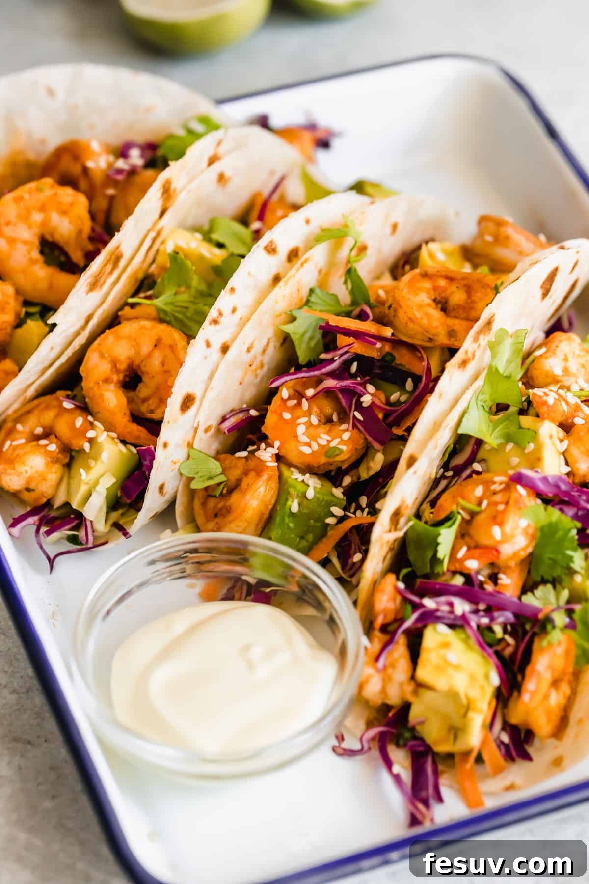 My easy shrimp tacos recipe with Asian cabbage slaw is guaranteed to be a new favorite. The classic flavors of a warm shrimp taco blend amazingly with the fresh, crunchy slaw in warm tortillas! A Platter Holding Four Shrimp Tacos and a Dish of Dressing